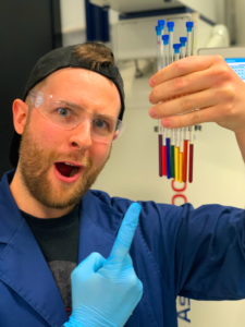 Liam Burt holding a hLiam Burt holding a handful of multicoloured chemicals in NMR tubesandful of multicoloured chemicals